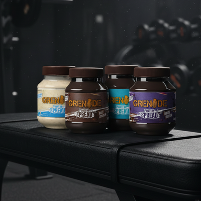 Four bottles of Grenade Protein Spread with different flavors on a dark surface.