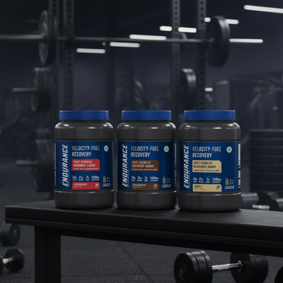 Three bottles of Endurance Velocity-Fuel Recovery Drink mix on a dark surface with a blurred gym background.