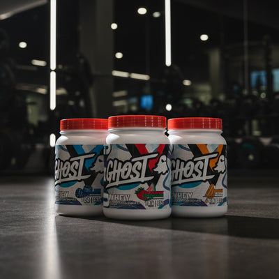 Three containers of Ghost whey protein powder on a gym floor.