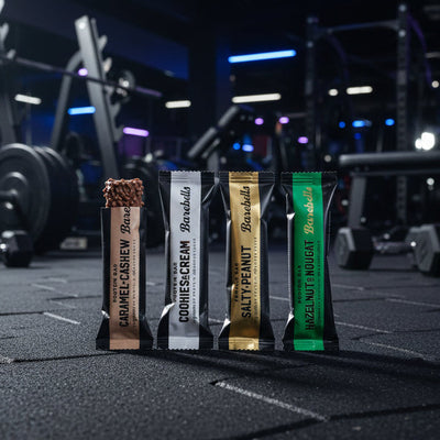 Five protein bars from Barebells with different flavors on a gym background.
