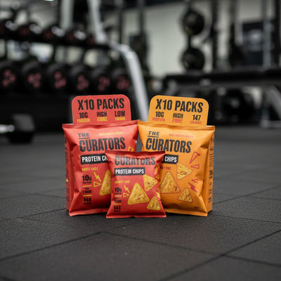 Packages of 'The Curators' protein chips on a gym floor with blurred gym equipment in the background.