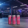 Three pink energy drink cans on a gym floor with equipment in the background