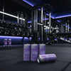 Three purple energy drink cans on a gym floor with gym equipment in the background