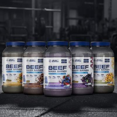 Five bottles of Beef Mass Gainer supplements on a dark surface with a gym background.