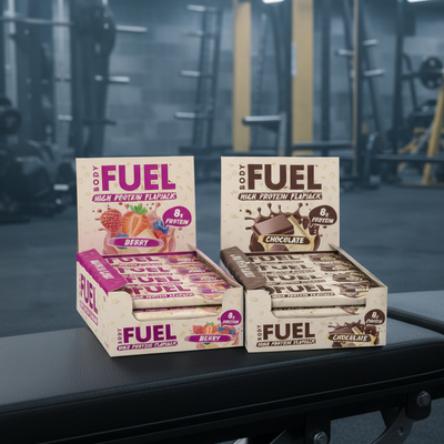 Boxes of Body Fuel high protein flapjacks in berry and chocolate flavors on a gym floor.