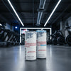 Two Red Bull energy drink cans on a gym floor with fitness equipment in the background.