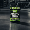 NXT Nutrition Amino Fuel supplement container on a dark surface with gym equipment in the background