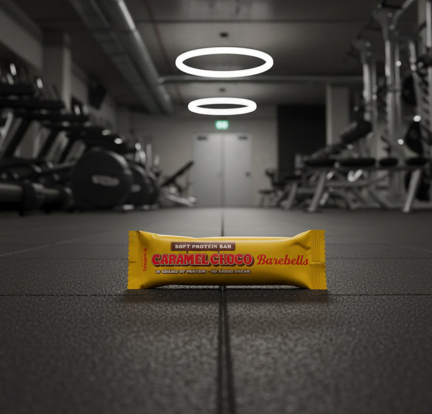 Caramel Choco Barachelis protein bar on a gym floor with equipment in the background