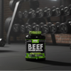 Beef protein isolate supplement bottle in a gym setting with weights in the background