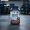 Beef mass gainer supplement container with Applied Nutrition branding on a gym background